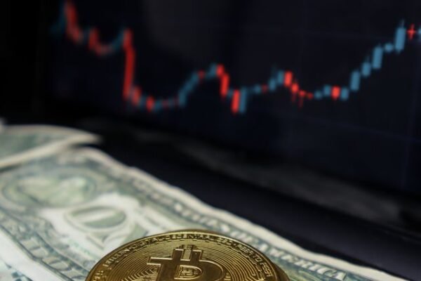 Bitcoin coin on US dollar bills with a stock market graph in the background.