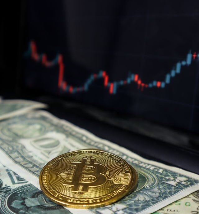 Bitcoin coin on US dollar bills with a stock market graph in the background.