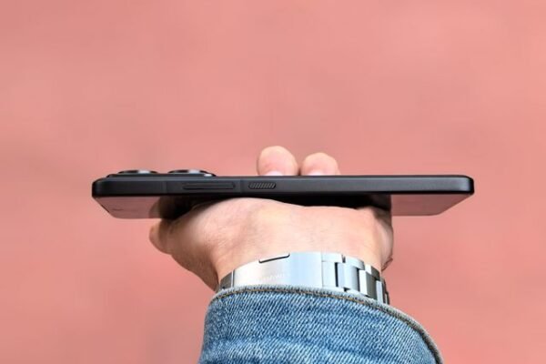 A person holding a smartphone horizontally against a soft pink backdrop, showcasing the device's slim profile.
