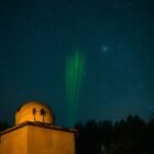 Observatory under starry sky with green laser beams pointing upwards.