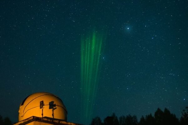Observatory under starry sky with green laser beams pointing upwards.