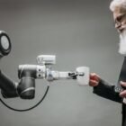 An elderly man receives a cup from a robotic arm in a modern office setting.